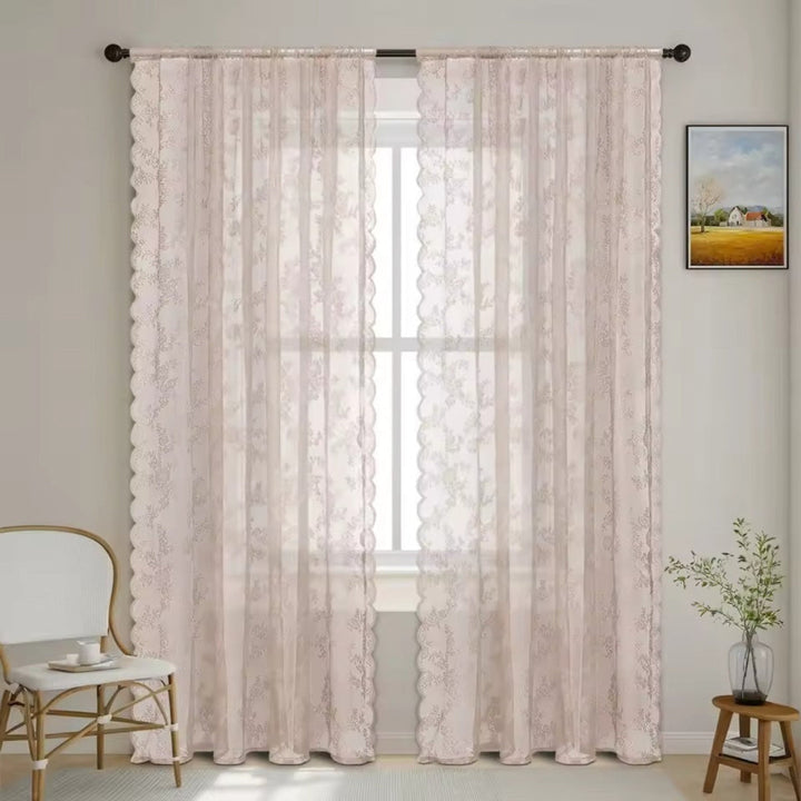 Pair of pale blush pink lace panels with scalloped edges hang from a dark rod beside a white chair.