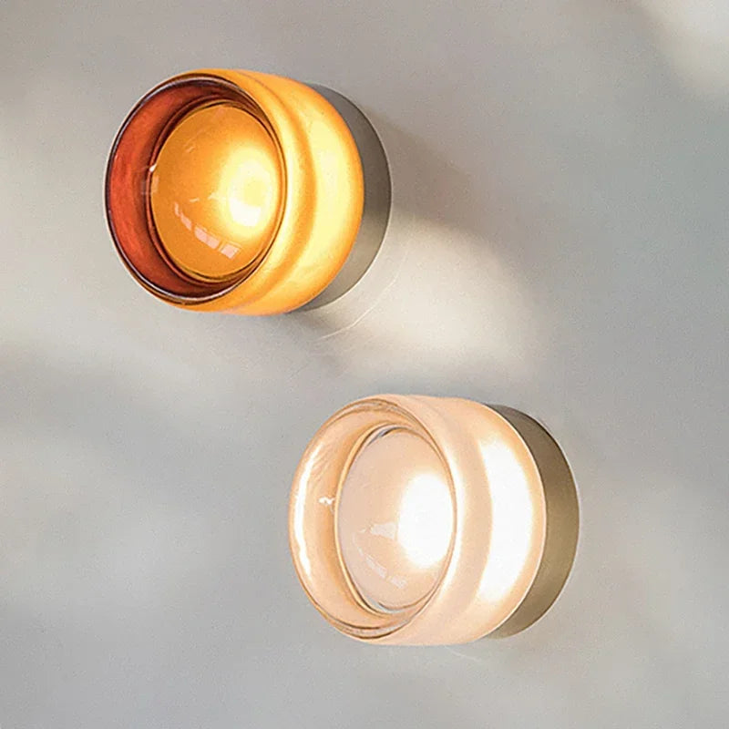 Close-up of two lit round glass wall lights, one amber and one clear frosted glass.