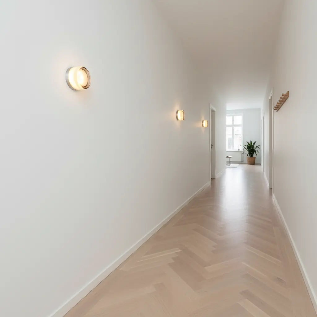Three round wall lights glowing along a bright hallway with a pale herringbone floor.