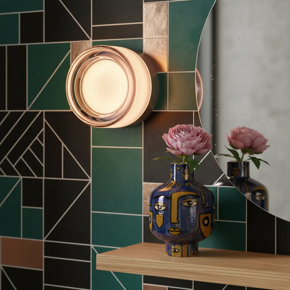 Round glass wall light detail on a green and black tiled wall with a rose-tinted rim.