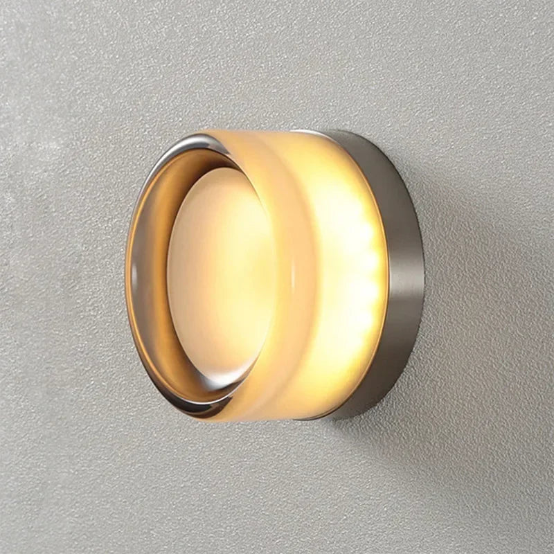 Side view detail of a lit round wall light with frosted glass body and clear rim.