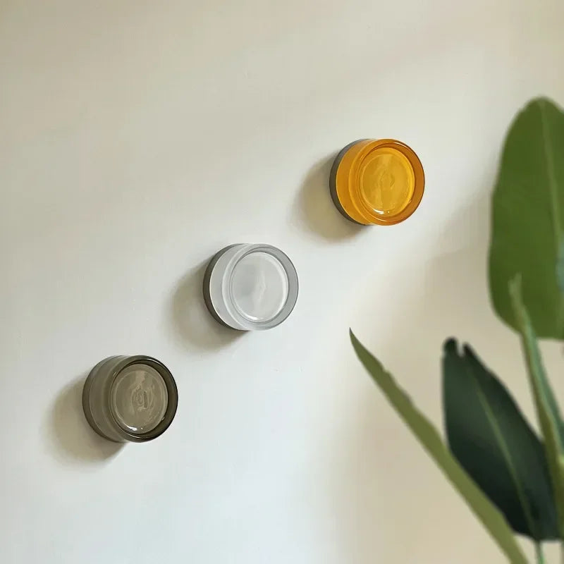 Three unlit round glass wall lights in amber, clear and smoky gray on a white wall.