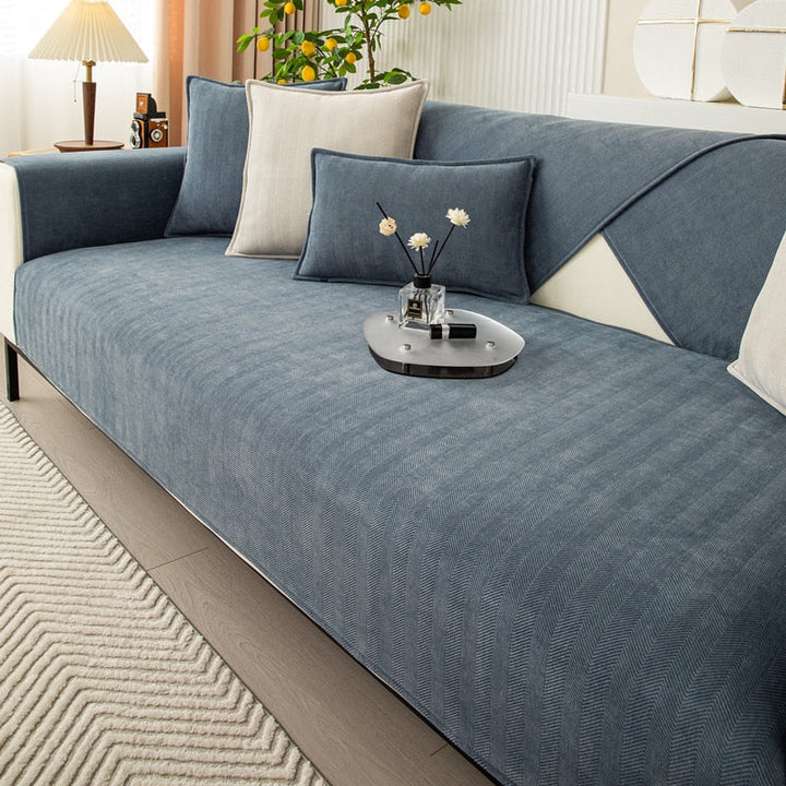 Dusty slate-blue chenille sofa cover on a sofa with blue and beige cushions and a decorative tray.