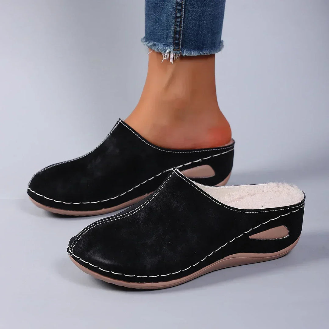 Black backless clog slippers with white stitching and a cutout in the sole, another view.