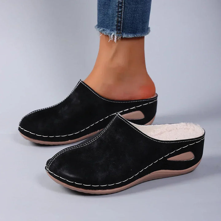 Black backless clog slippers with white stitching and a cutout in the sole, another view.