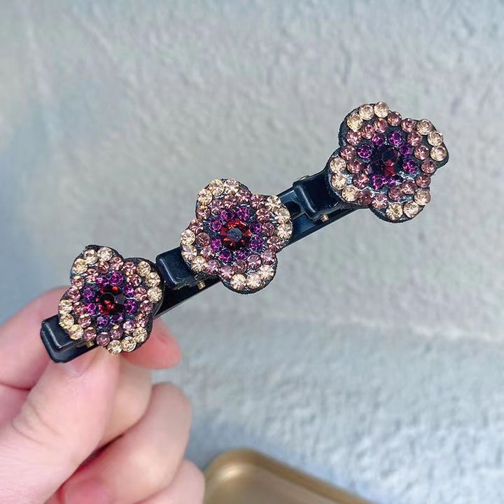 Close-up of a hand holding one black clip with three purple and gold rhinestone flowers 2