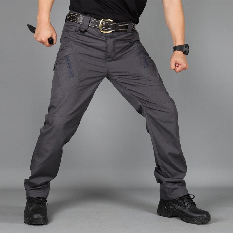 Men's dark gray cargo pants front view on a model in a wide stance with zippered thigh pockets and a belt.