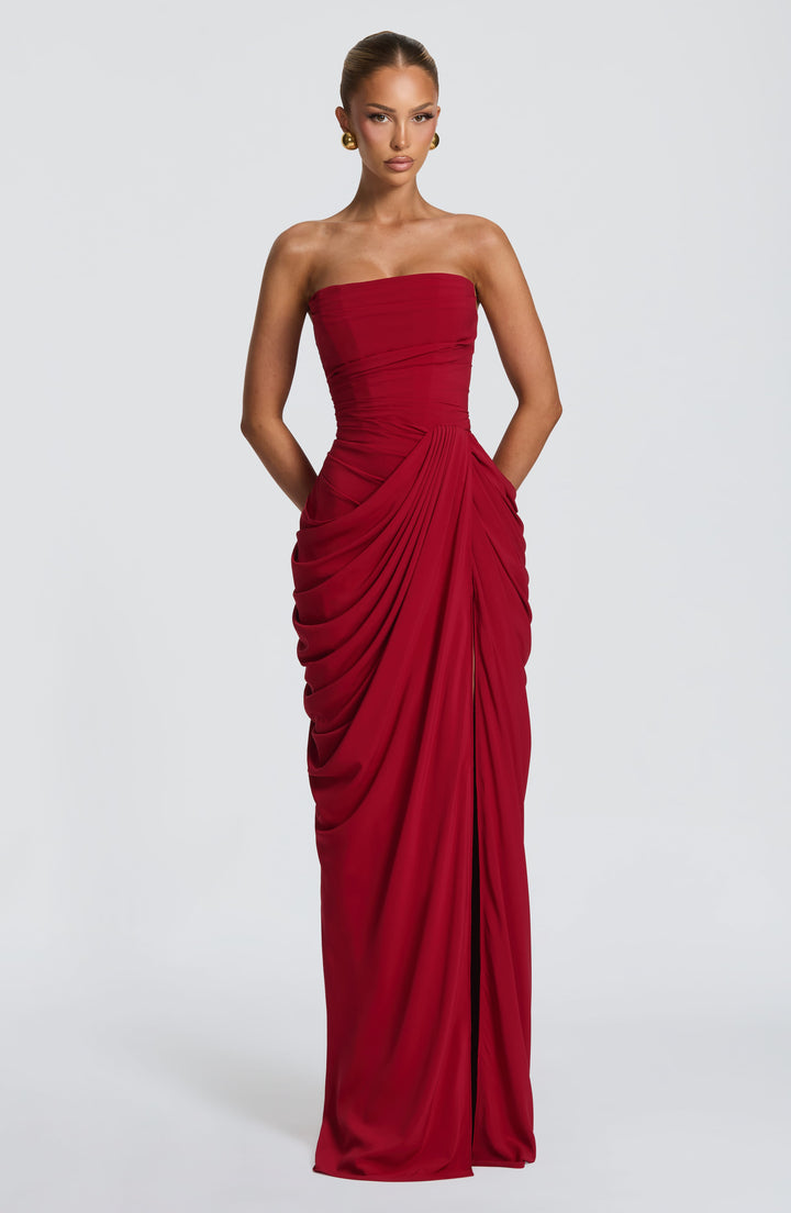 Red strapless corset maxi dress with draped wrap skirt, front view with hands in pockets and a side slit. 27