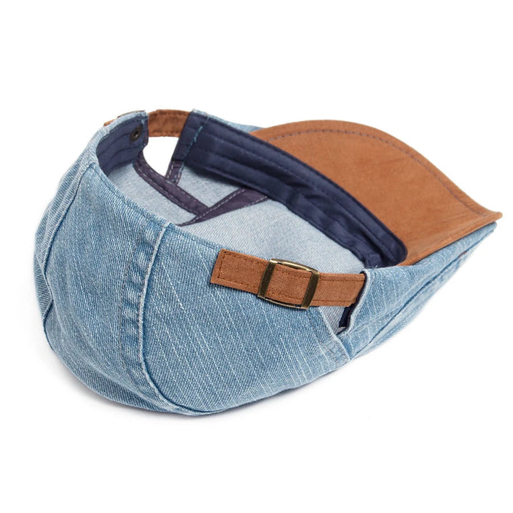 Men's flat cap shown upside down with navy lining, tan brim underside and brass buckle.