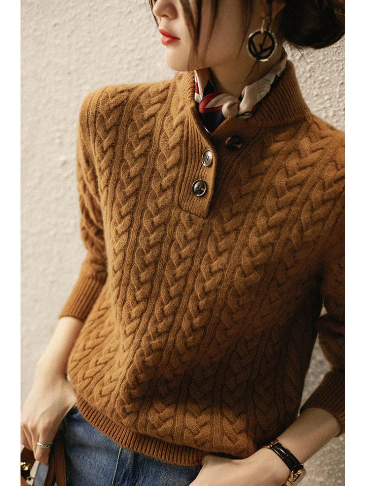 Model leaning against a textured wall in the caramel brown cable-knit sweater, showing the button placket and ribbed cuff. 4