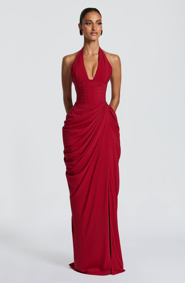 Model in the red halter maxi dress facing front on a plain studio backdrop, showing the plunging neckline, corset waist and draped skirt. 21
