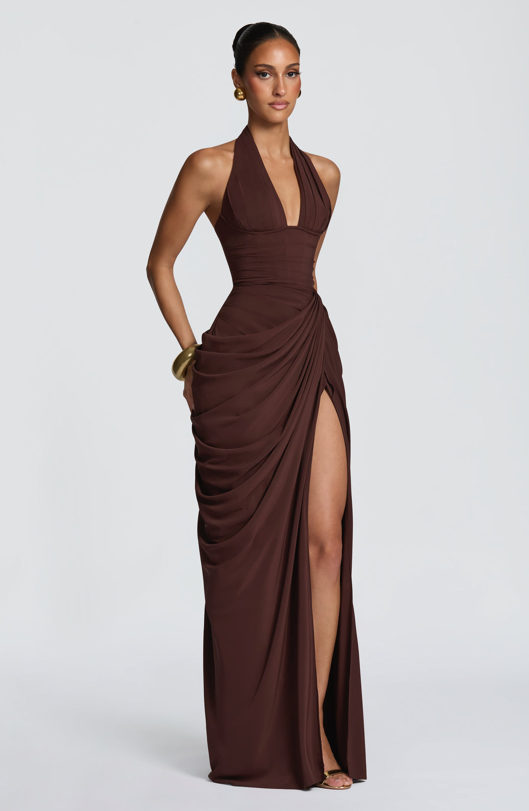 Three-quarter view of the brown halter maxi dress with a gold bangle, showing the high slit and side drape. 27