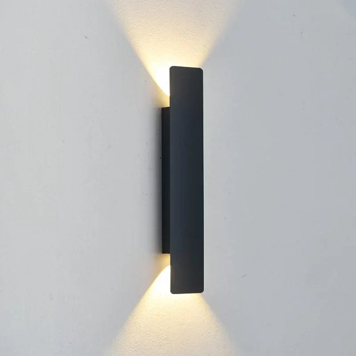 Single black rectangular wall light mounted on a pale wall, with warm light beaming upward and downward.