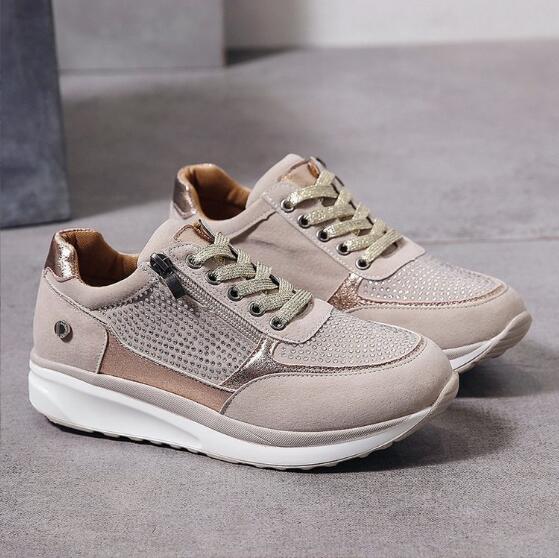 Pair of beige sneakers with sparkly gold laces, studded side panel, zipper and thick white sole, shown on a gray floor. 2