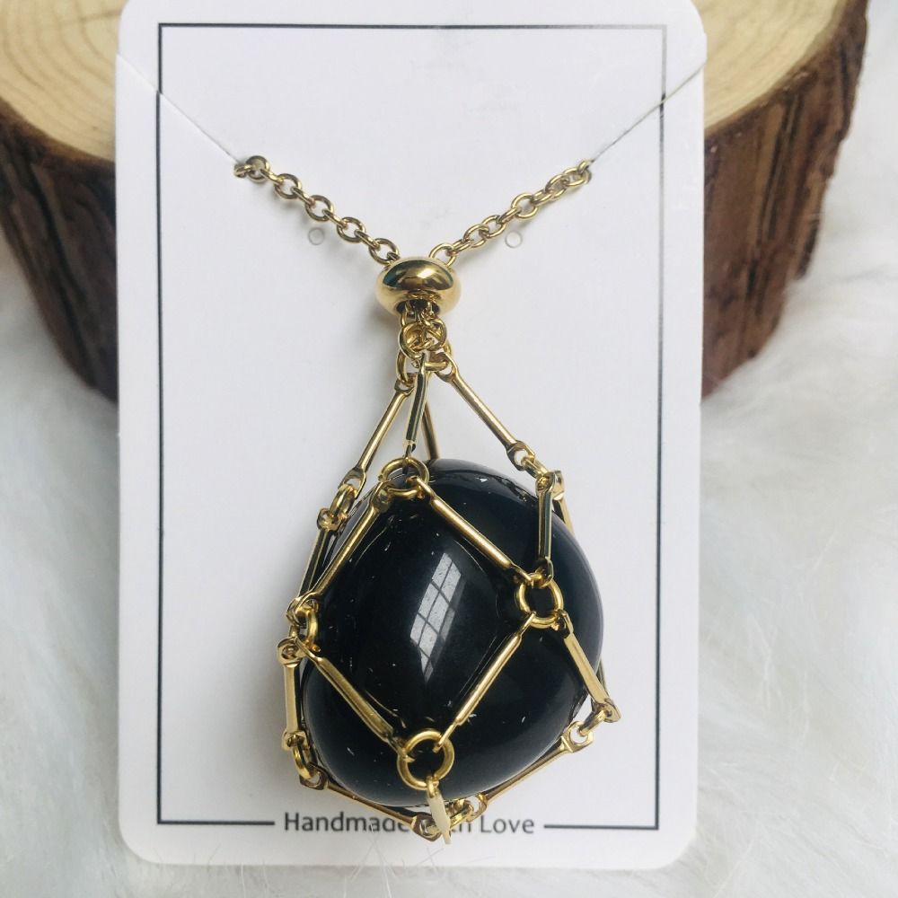 Gold cage necklace with a glossy black stone on a white card in front of a wood log slice. 7
