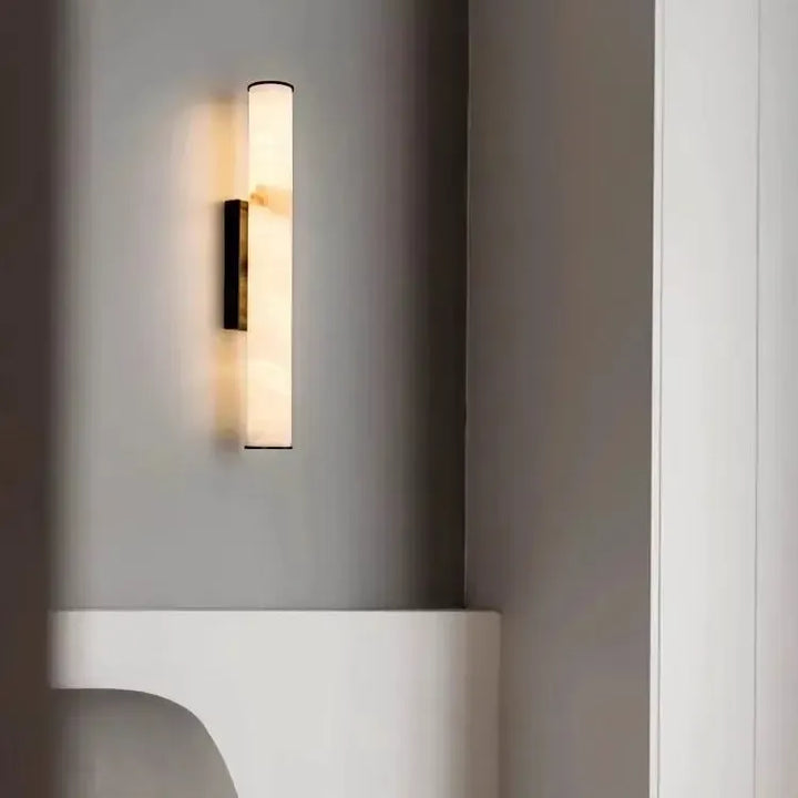 Dark-finish marble sconce lit on a gray wall above a curved white built-in shelf, with a white doorframe at the right.