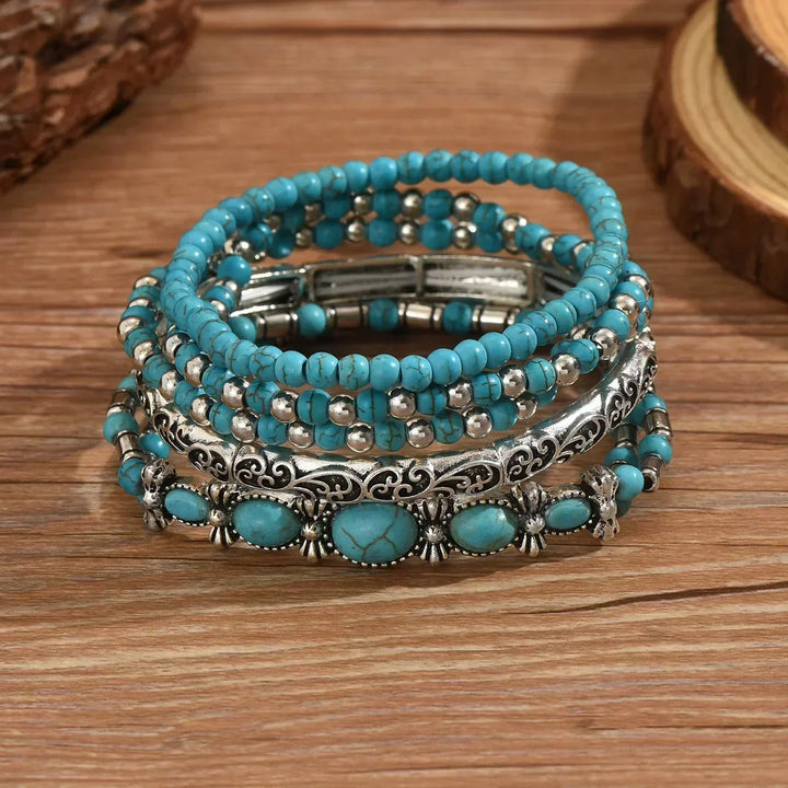Five stretch bracelets stacked on a wooden surface, showing round turquoise beads, silver spacers, a scrolled bangle and a stone cuff. 3