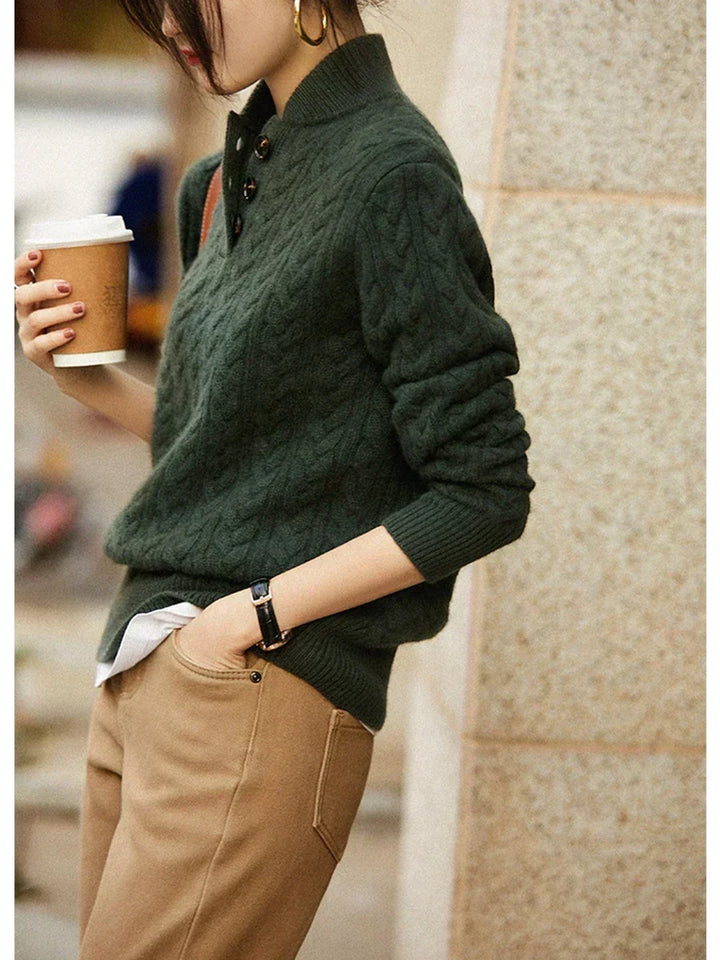 Model holding a coffee cup in the dark green cable-knit sweater with buttoned collar, worn with camel trousers and a watch. 8