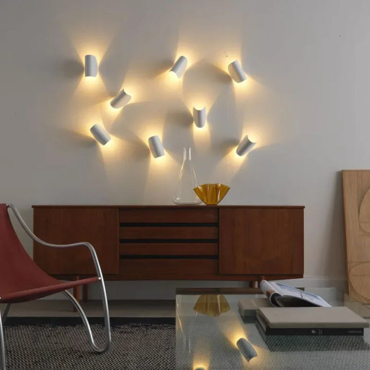Cluster of white wall lights set at varied angles on a wall above a wooden sideboard, forming a glowing pattern.