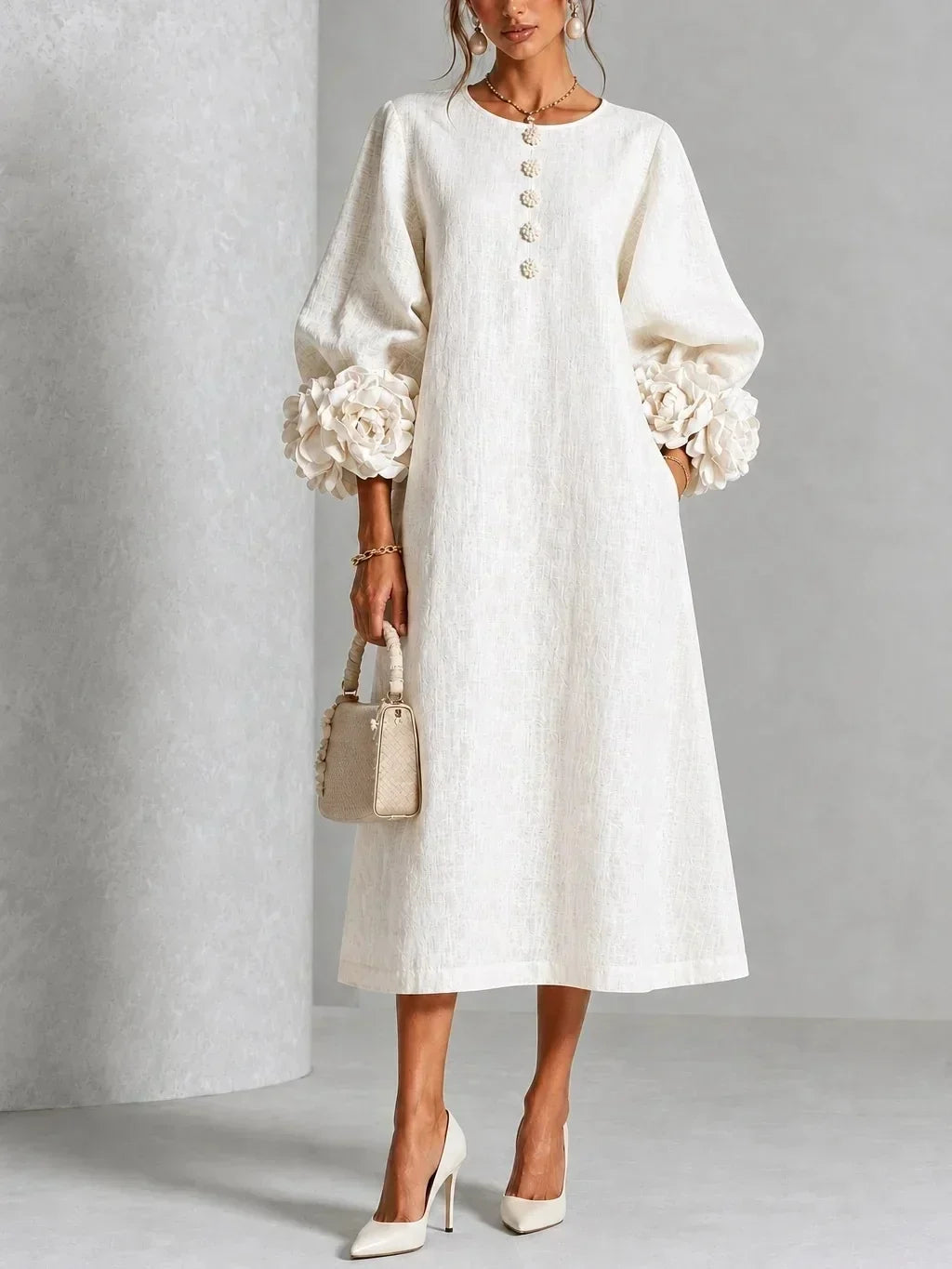 Model wears the cream white midi dress with puffed sleeves, rose-shaped cuffs and floral buttons, styled with ivory heels and a woven bag. 1