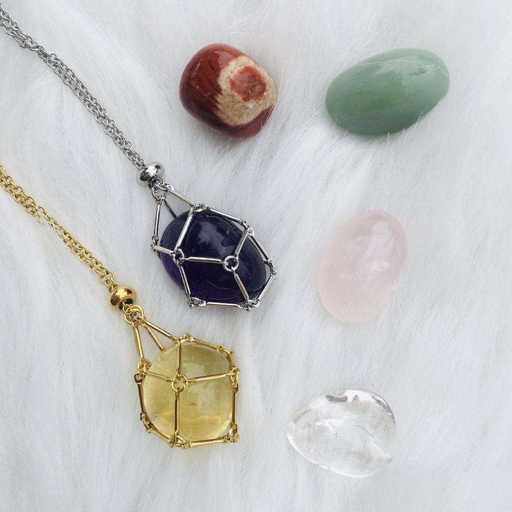 Another view of gold and silver cage necklaces with yellow and purple stones beside loose tumbled stones. 2