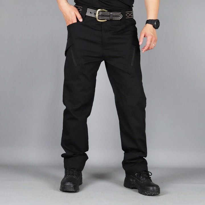 Men's black cargo pants front view on a model with one hand in a pocket, worn with a belt and black boots.