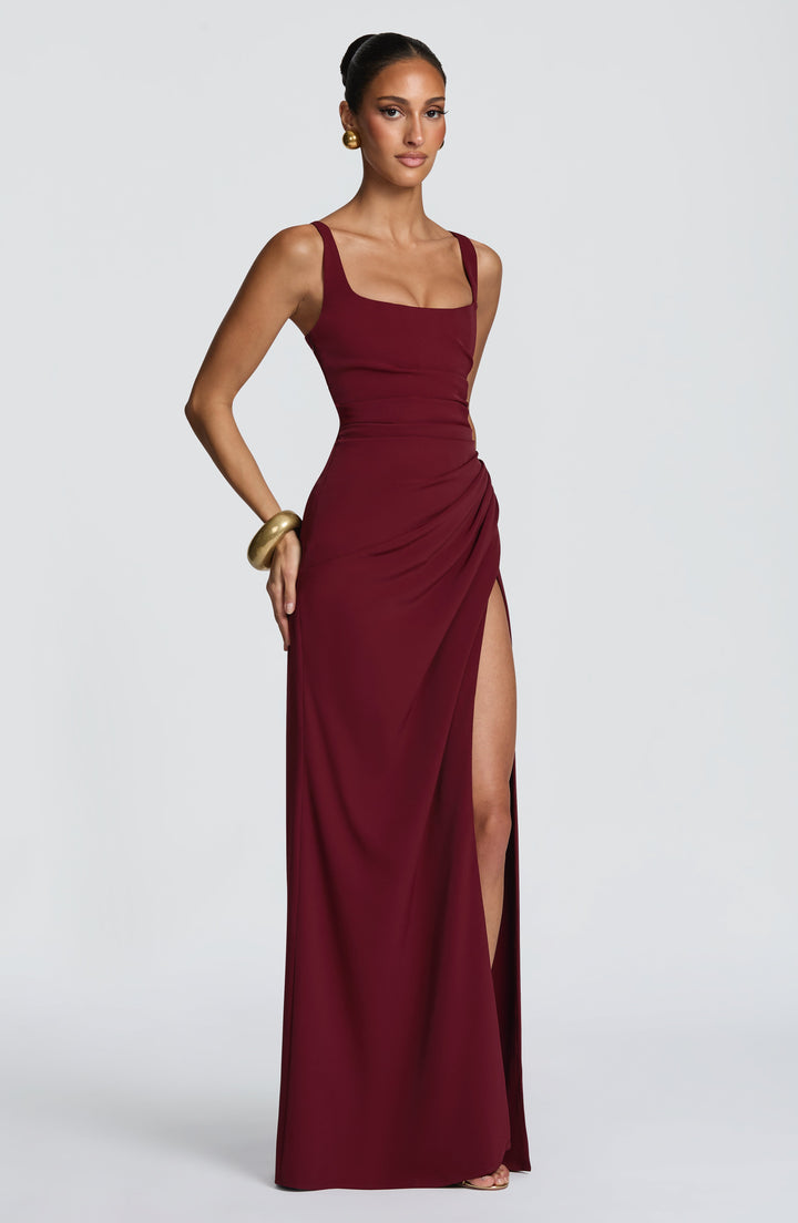 Burgundy Camille Maxi Dress on a model with one hand on her hip, showing the ruched hip drape and high slit.