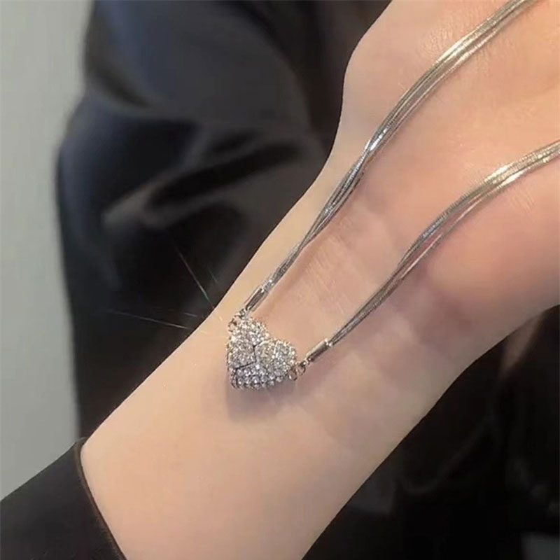 The silver multi-strand necklace laid across a wrist, with the rhinestone heart closed at the center and sparkling in the light. 7