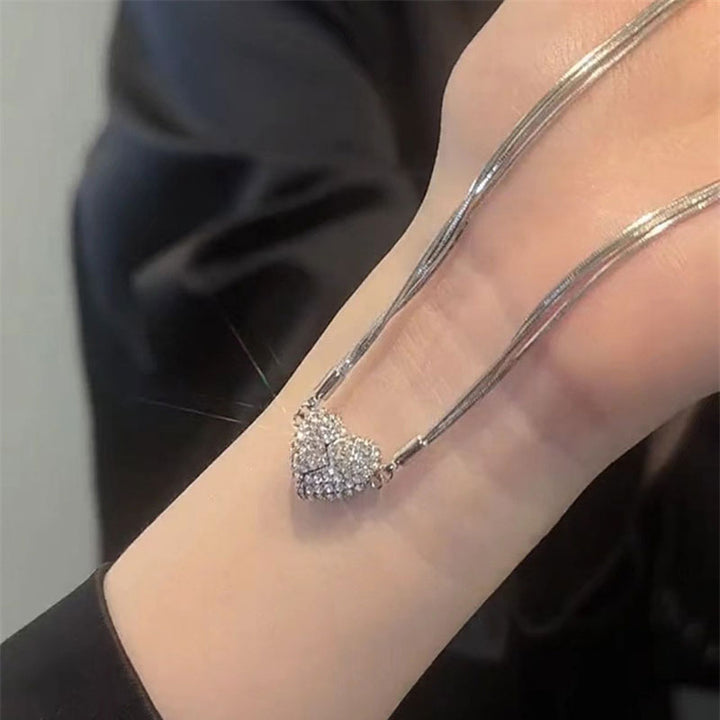 The silver multi-strand necklace laid across a wrist, with the rhinestone heart closed at the center and sparkling in the light. 7
