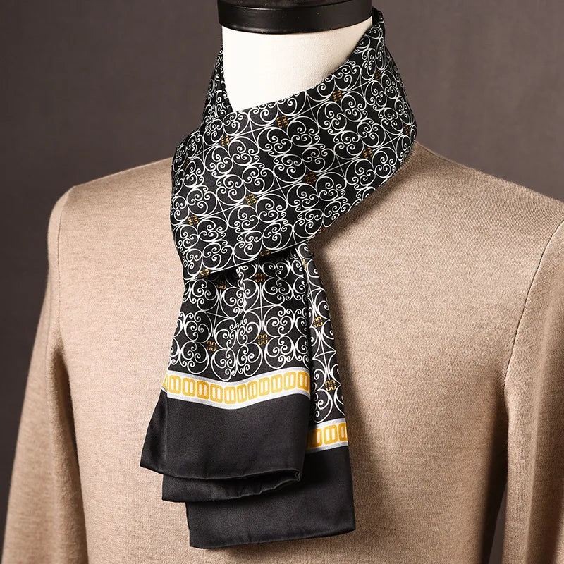 Black silk scarf with white scrollwork pattern and a gold chain-link border, draped on a mannequin wearing a tan sweater. 25