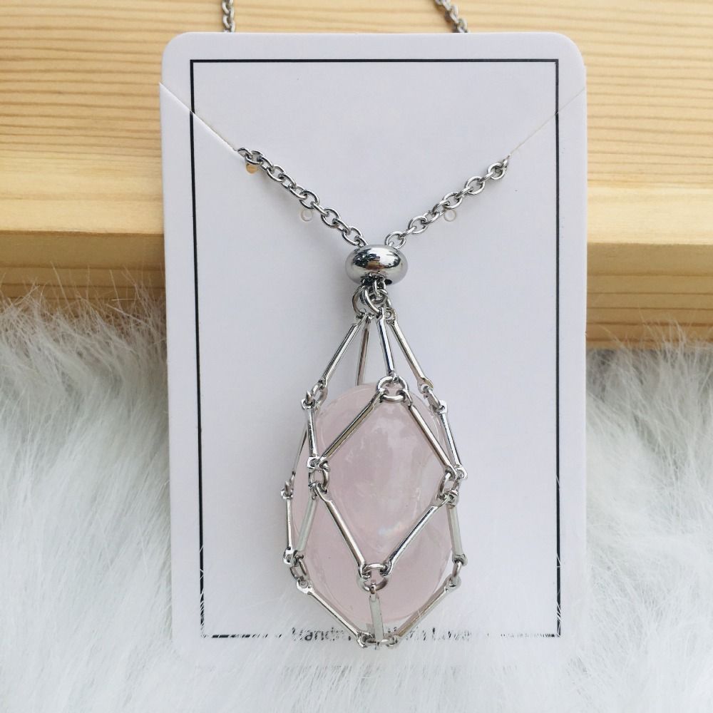 Silver cage necklace with an oval light pink stone on a white card against a wood plank and white fur. 11