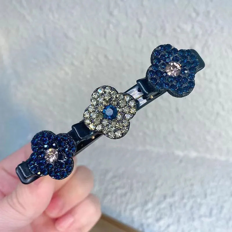 Hand holding a black clip with three rhinestone flowers in deep blue and gray tones 3