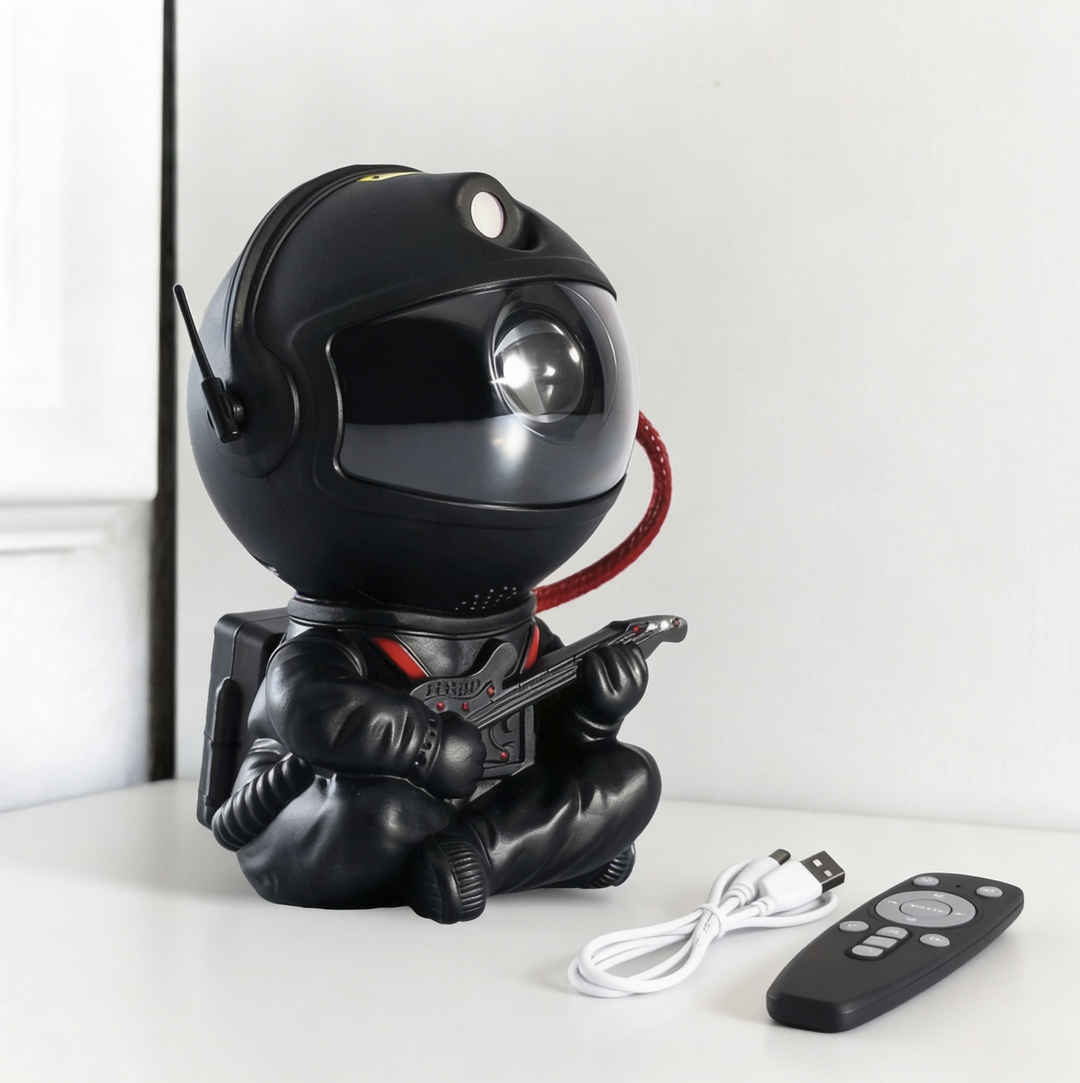 Black guitar-playing astronaut projector shown from an angle with its backpack, a white USB cable and a black remote beside it.