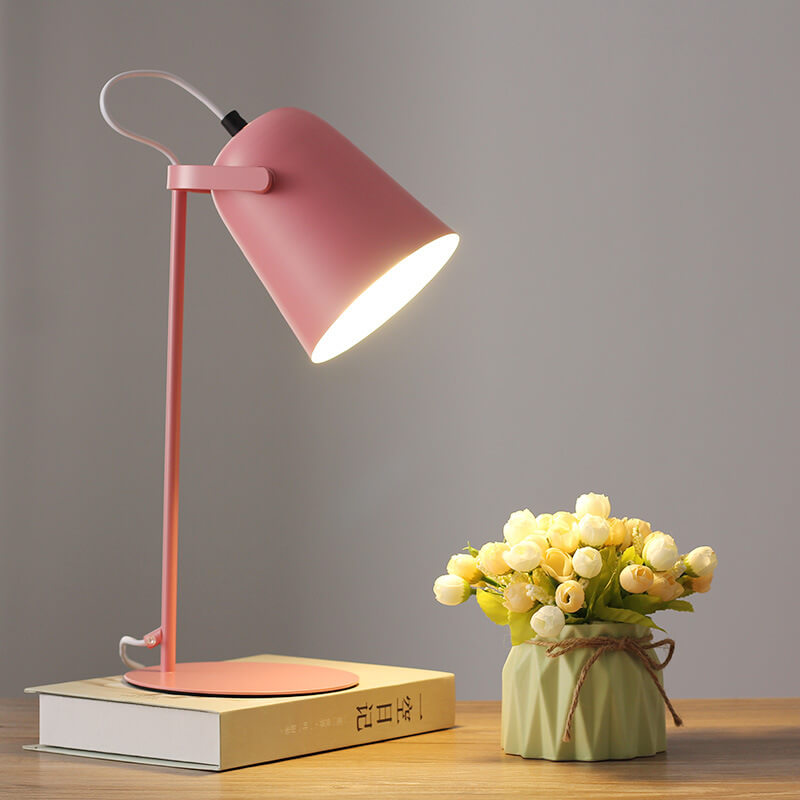 Pink version of the lamp glowing on a book beside a vase of cream flowers 8