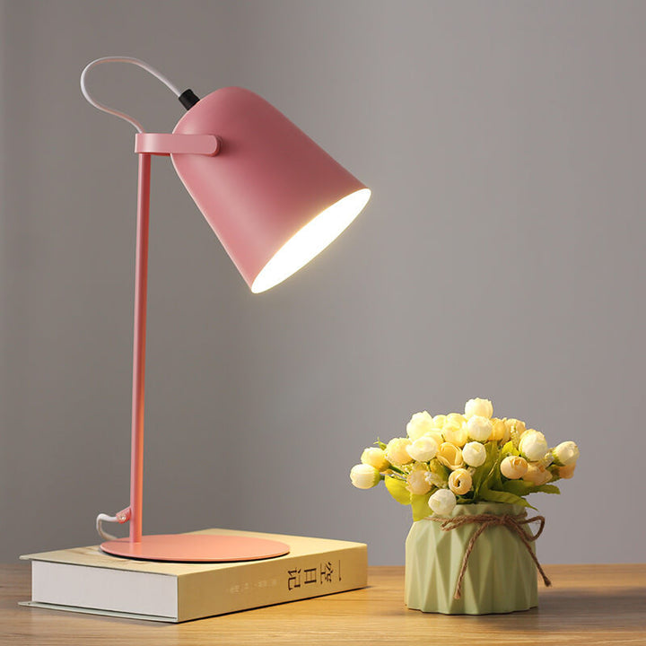Pink version of the lamp glowing on a book beside a vase of cream flowers 8