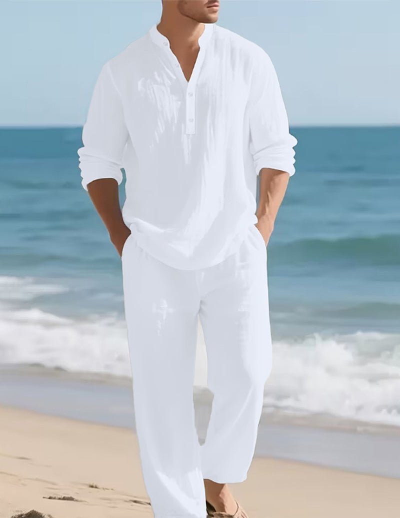 Men's white linen set, another view on a sandy beach with hands in pockets.