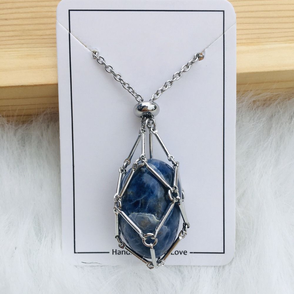 Silver cage necklace with an oval blue stone with white veining on a white card against wood and fur. 13