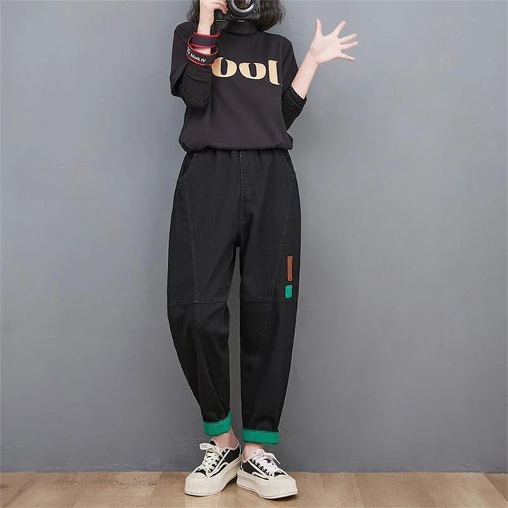 Frau in schwarzem "Cool"-Shirt und schwarzer Hose mit grünen Details, lässiger Stil.