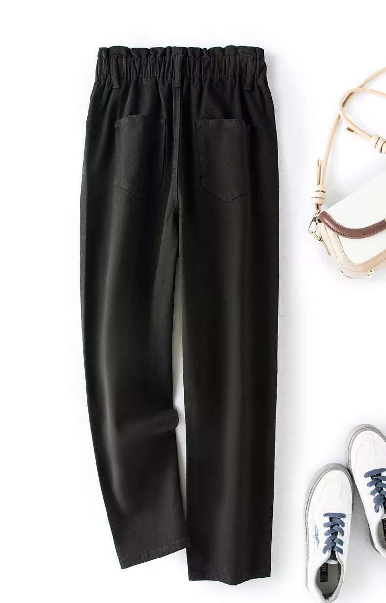 Schwarze Damenhose mit elastischem Bund, Taschen, aus Baumwolle, neben weißen Sneakers und Tasche.