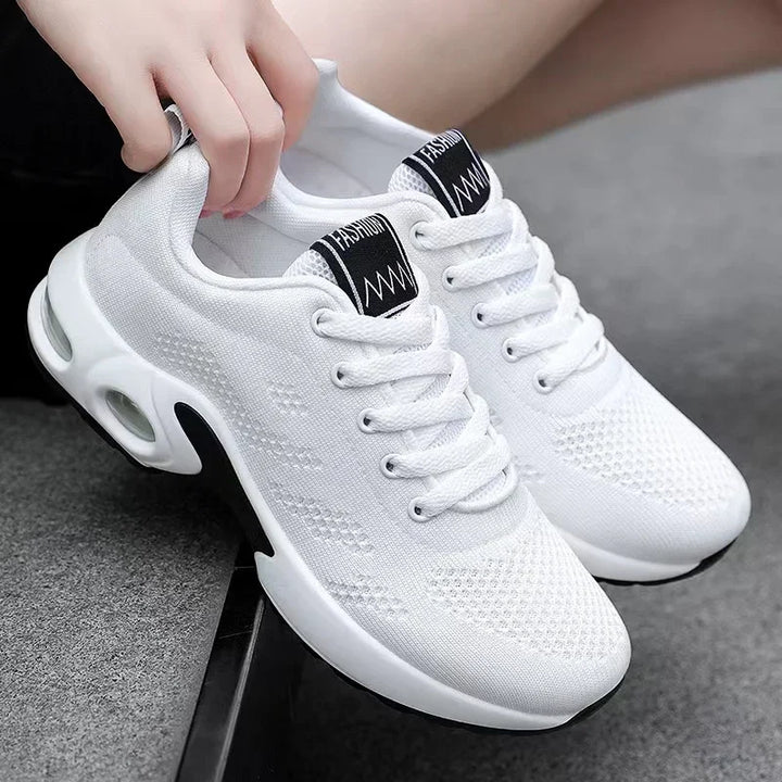 Pair of white knit sneakers with air-cushion soles, one shoe held by hand.