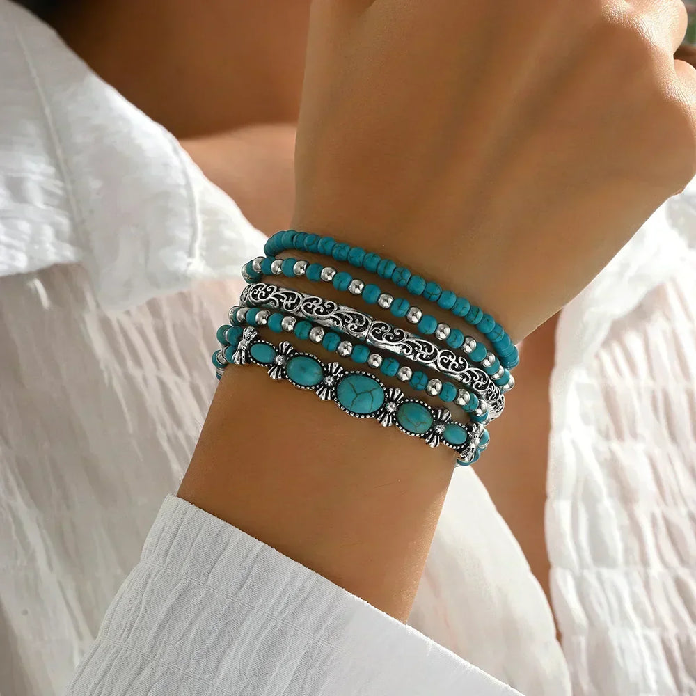 Model's raised wrist wearing the stack of five bracelets, showing turquoise beads, a filigree silver bangle and an oval stone cuff. 2