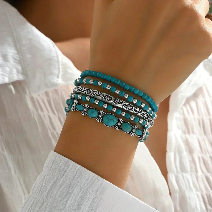 Model's raised wrist wearing the stack of five bracelets, showing turquoise beads, a filigree silver bangle and an oval stone cuff. 2