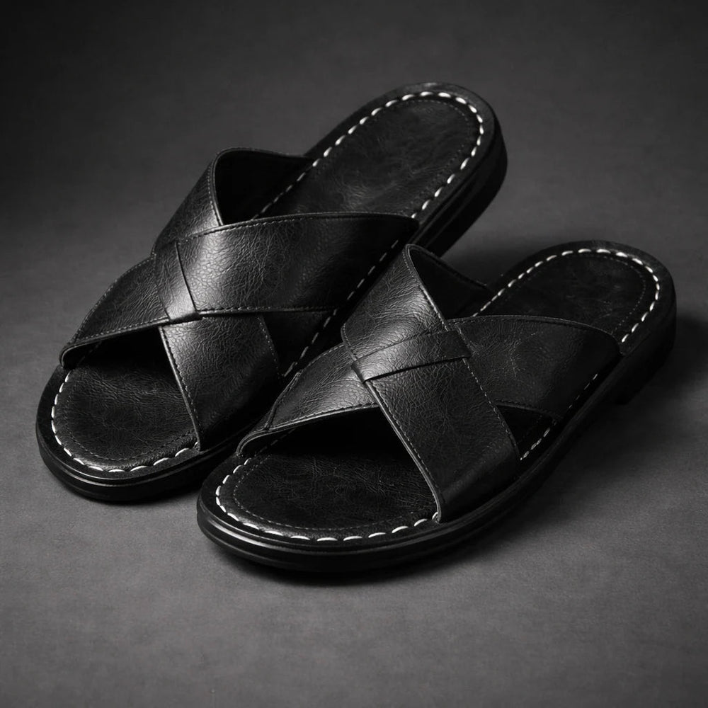 Pair of black crossed-strap slide sandals with white contrast stitching, shown at an angle on a dark gray surface. 2