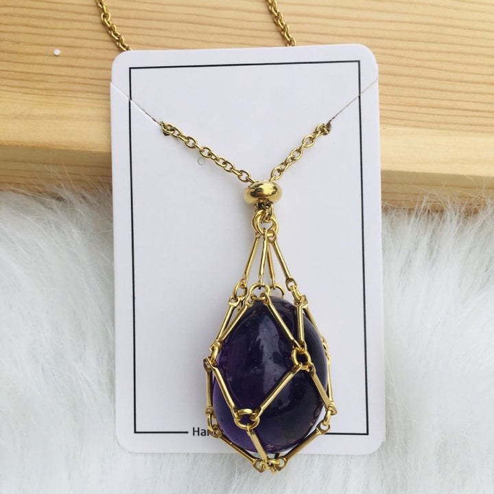 Gold cage necklace with an oval deep purple amethyst stone on a white card against wood and white fur. 16