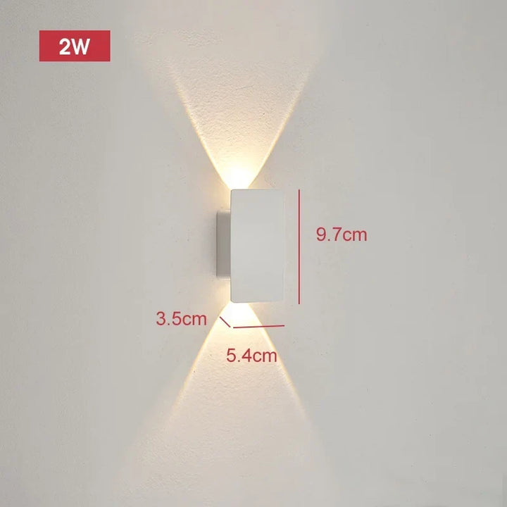 Smallest white wall light on a pale wall projecting narrow beams up and down, with dimension lines marking its size.