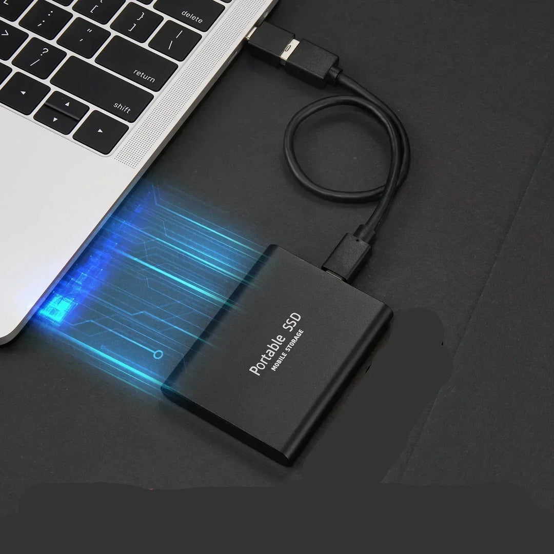 Black portable SSD connected by a short cable to a silver laptop, detail.