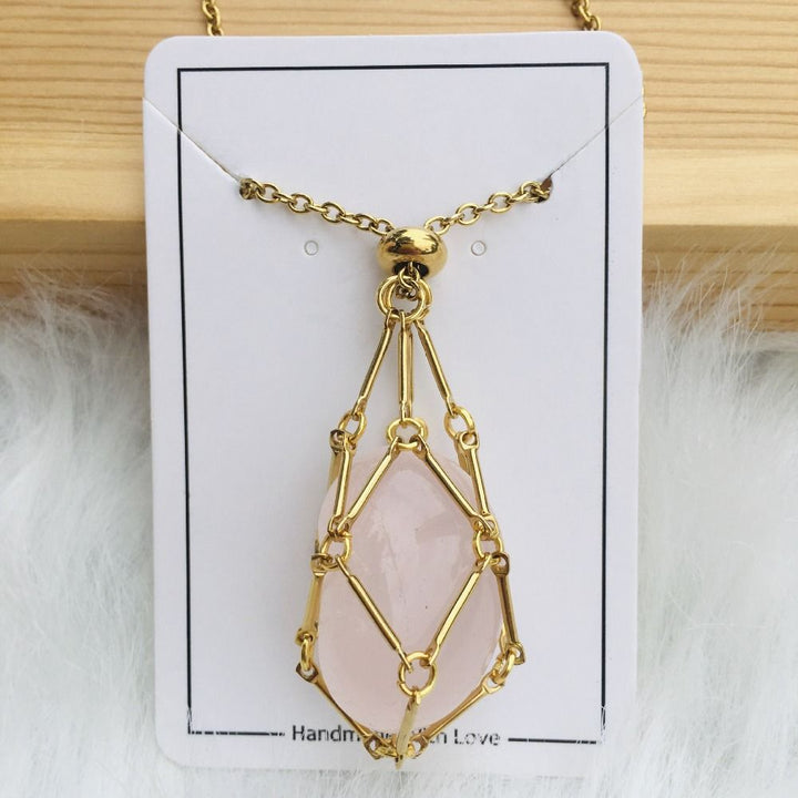 Gold cage necklace with an oval light pink rose quartz stone on a white card on wood and fur. 10