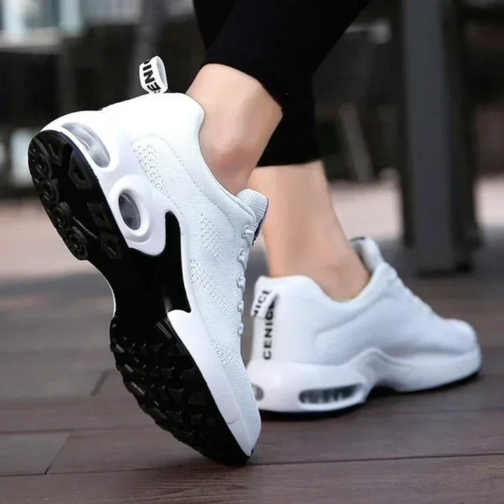 Rear and sole view of white knit sneakers with black tread and transparent heel air cushion.