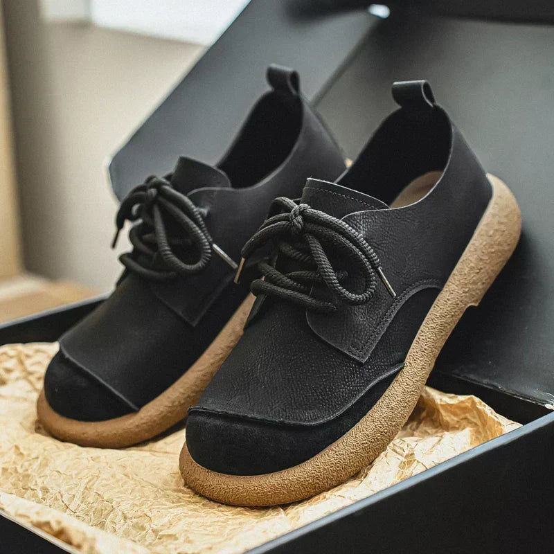Pair of black lace-up shoes with textured leather uppers and thick tan crepe soles.