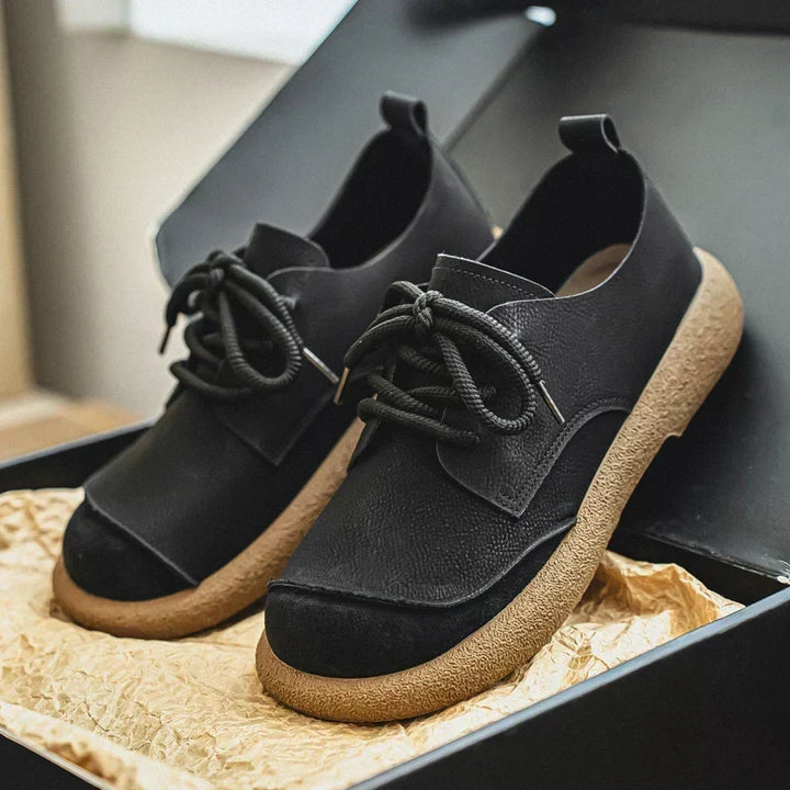 Pair of black lace-up shoes with textured leather uppers and thick tan crepe soles.